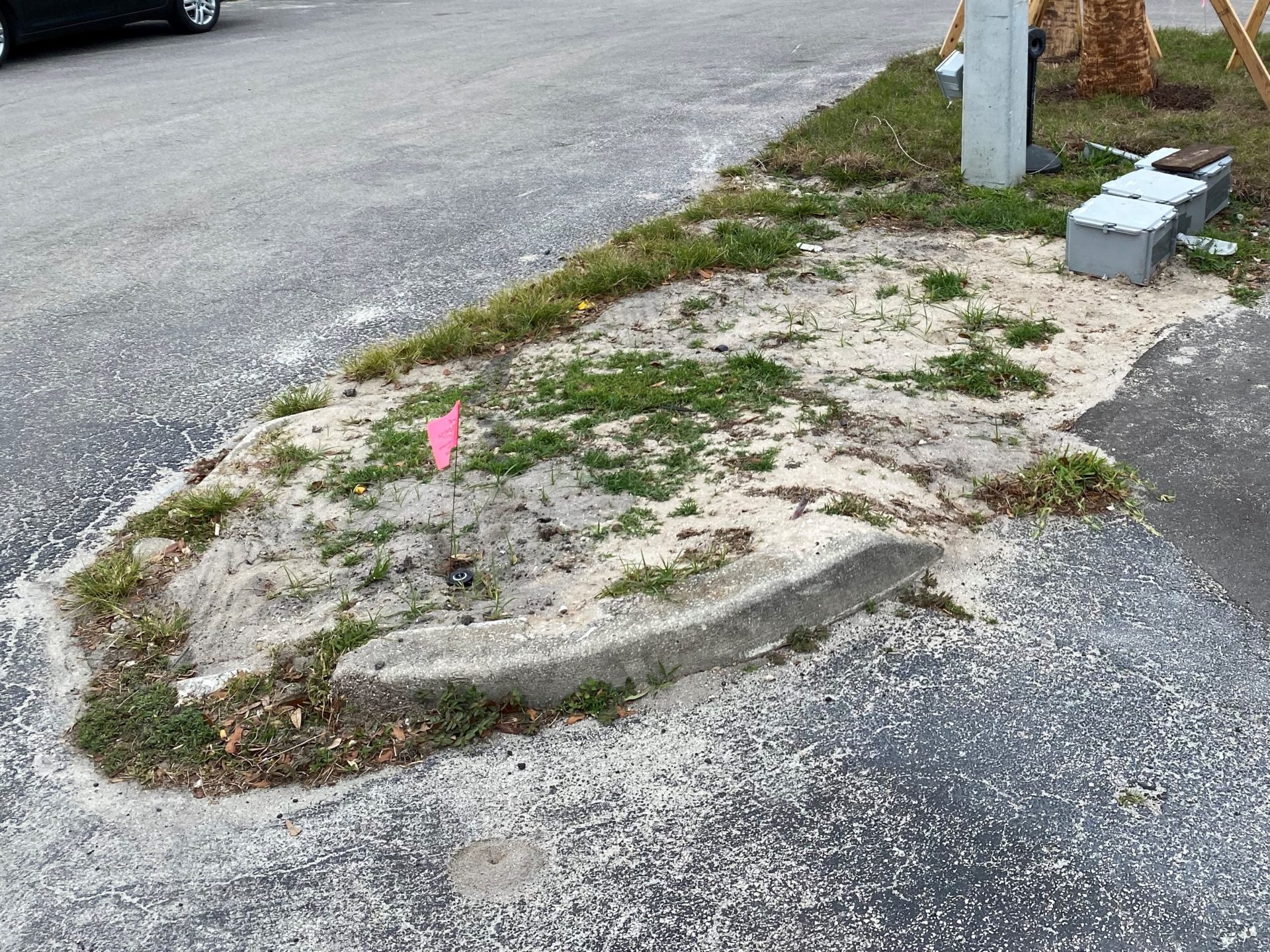 An island of dead grass at a dealership lot because the sprinkler head isnt working.