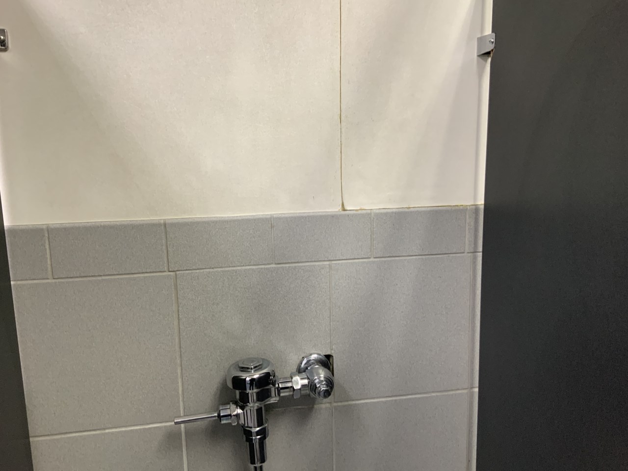 Wallpaper peeling and hole around urinal plumbing in dealership bathroom