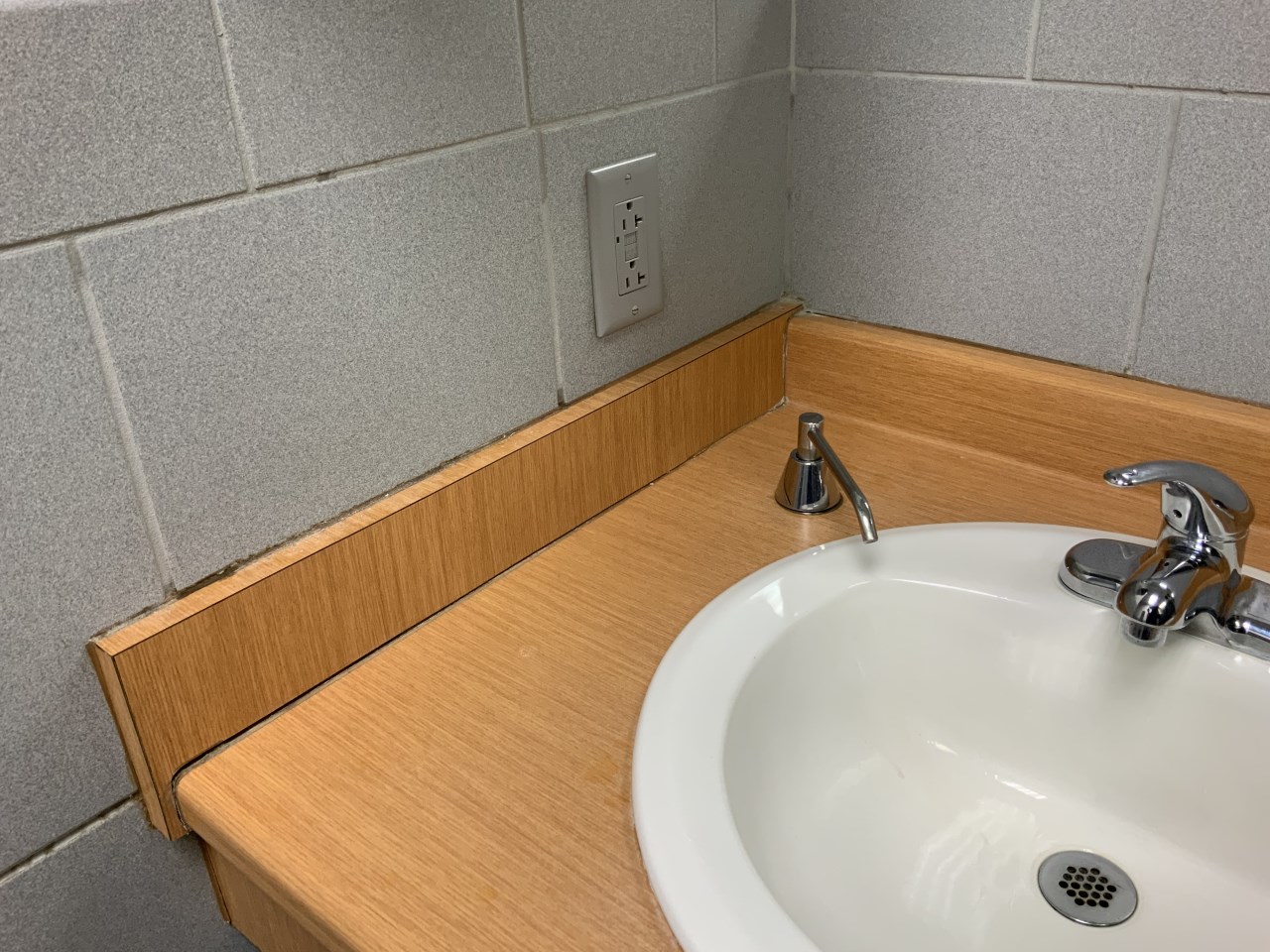 Tired sink area with dirty grout and caulking in dealership bathroom